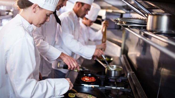 Fotografia della cucina di un ristorante. Brigata di cucina: chef, sous chef e commis a lavoro.